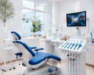 Bright modern treatment room with a blue dental chair, instrument tray and wall-mounted screen
